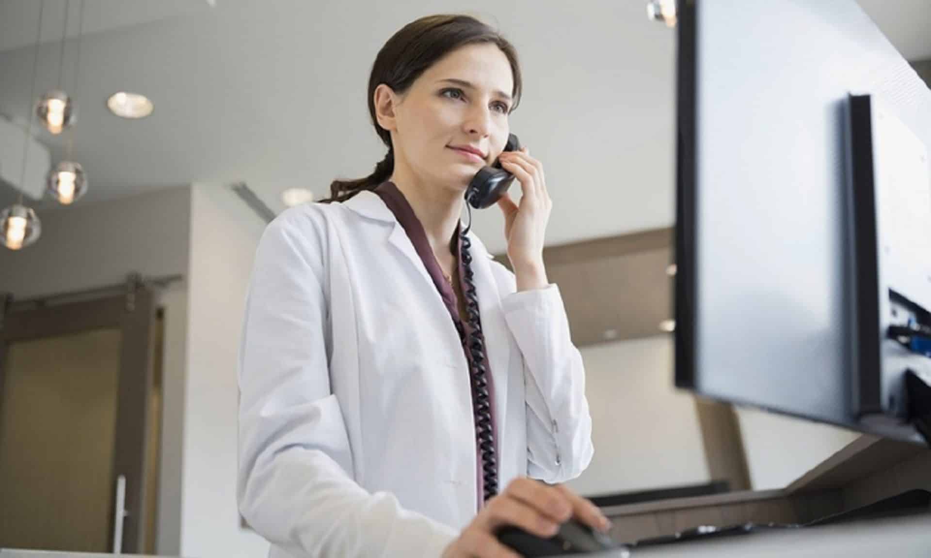 zdjęcie rejestratorki medycznej rozmawiającej przez telefon, klikającej w komputerze