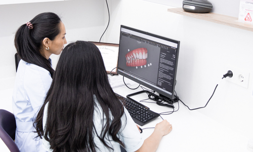 Dwie osoby analizują projekt dentystyczny na ekranie komputera, w otoczeniu dokumentów.