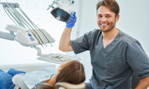 Dentysta z pacjentką na fotelu trzyma lampę dentystyczną w gabinecie.